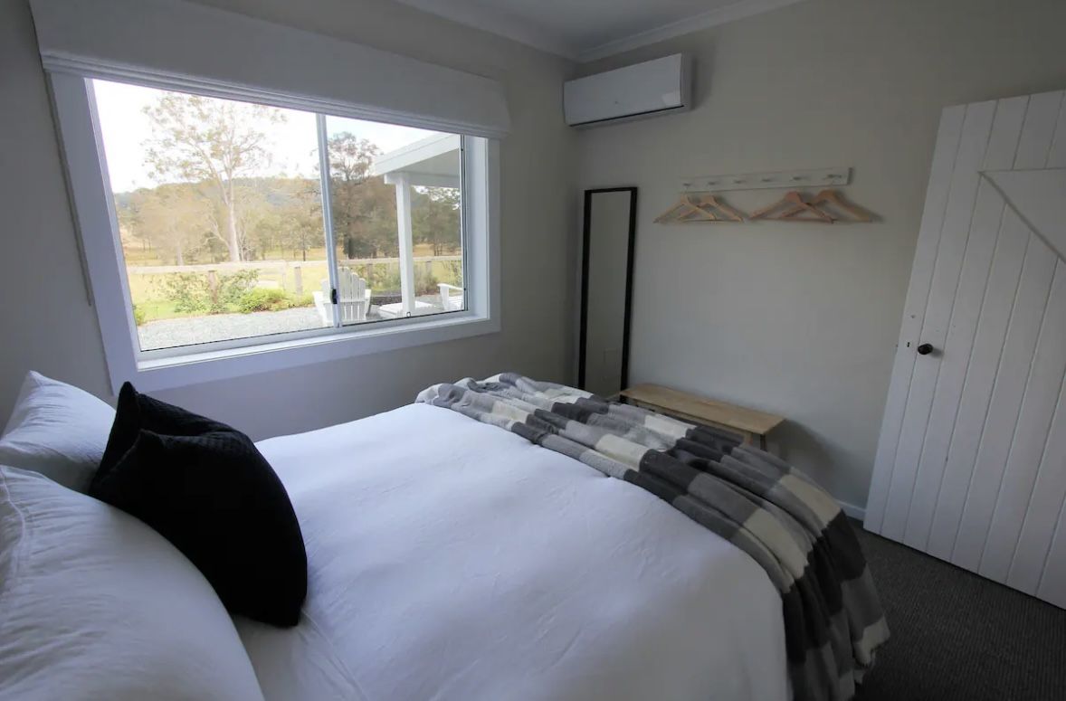 Queen bedroom with white linen and a paddock view in the Nabiac cottage